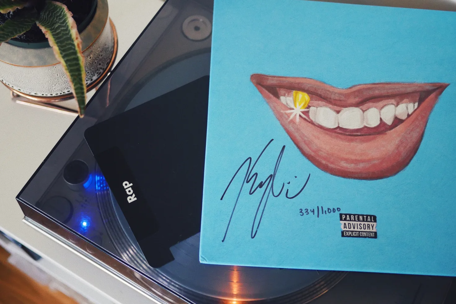 A black Rap divider resting on a turntable beside a signed, numbered LP whose blue cover shows a painted smile with a gold tooth