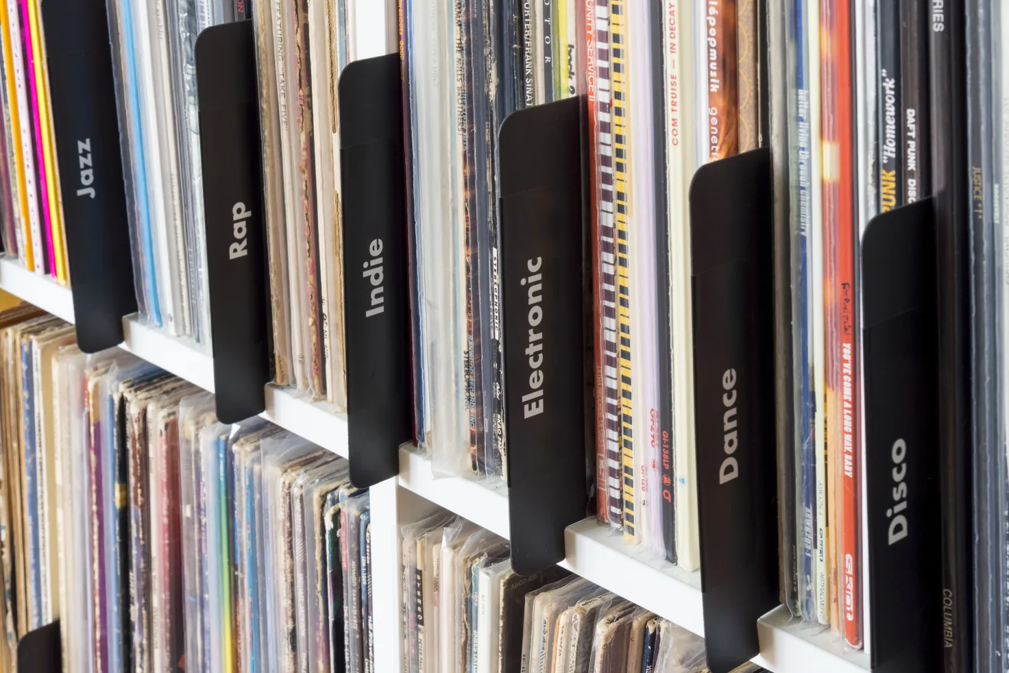 Black dividers in use on a white record shelf, their tabs labeled Jazz, Rap, Indie, Electronic, Dance, and Disco between rows of LPs