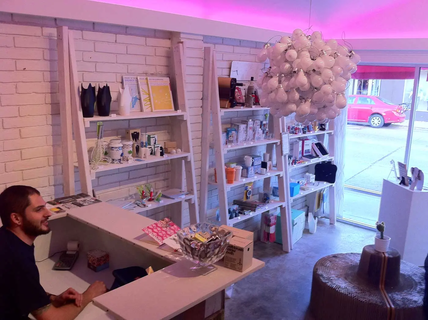 The Sirtified retail shop — white ladder shelving of design goods, a light-bulb chandelier, and the checkout counter